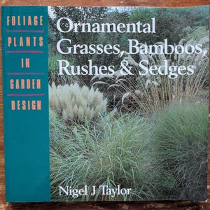 Może przedstawiać: Książka zatytułowana "Ornamental Grasses, Bamboos, Rushes & Sedges" autorstwa Nigela J Taylora. Okładka przedstawia zdjęcie różnych traw i roślin. Grzbiet jest turkusowy i zawiera napis "Foliage Plants In Garden Design".