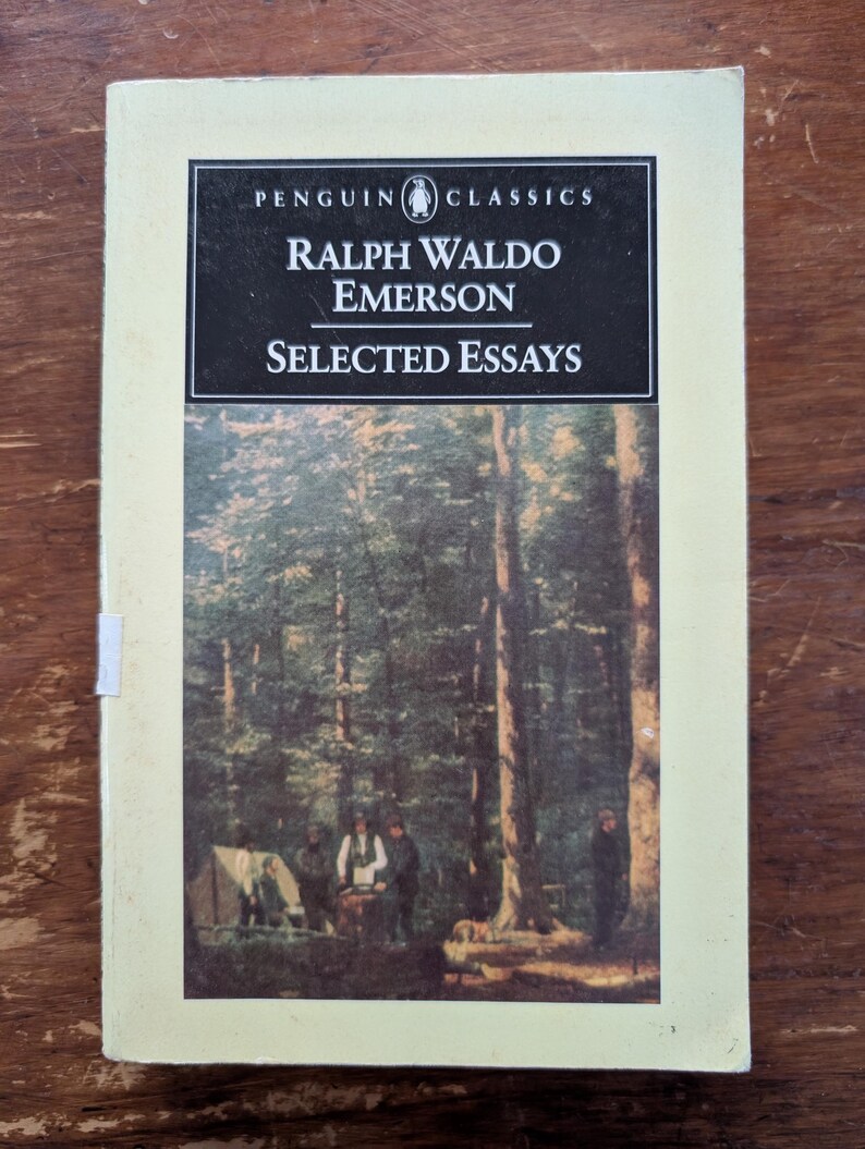 K&ouml;nnte beinhalten: Ein Penguin Classics Taschenbuch mit einem schwarz-wei&szlig;en Cover mit dem Titel "Ralph Waldo Emerson Selected Essays". Das Cover zeigt auch eine Schwarzwei&szlig;illustration einer Gruppe von Menschen in einer Waldlandschaft.
