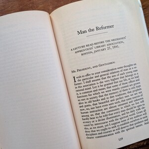 K&ouml;nnte beinhalten: Eine Seite aus einem Buch mit dem Titel "Der Mensch, der Reformer" mit dem Text "Ein Vortrag, gehalten vor der Mechanics' Apprentices' Library Association, Boston, am 25. Januar 1841." Der Text auf der Seite behandelt die Rolle eines Reformers in der Gesellschaft.