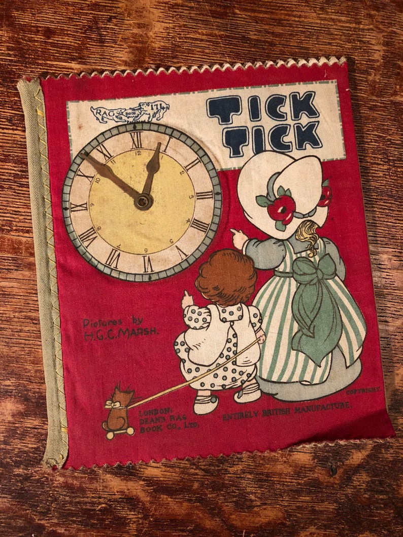 Puede incluir: Un libro de tela rojo con una esfera de reloj en la portada. El libro se titula "Tick Tick" y presenta a dos ni&ntilde;os, uno de los cuales lleva un gato con una correa. El libro est&aacute; hecho por Dean's Rag Book Co. Ltd. y es completamente de fabricaci&oacute;n brit&aacute;nica.