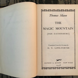Puede incluir: Una cubierta de libro vintage con un diseño en blanco y negro. El título es "La Montaña Mágica" de Thomas Mann. El libro fue publicado en 1948 por Alfred A. Knopf.