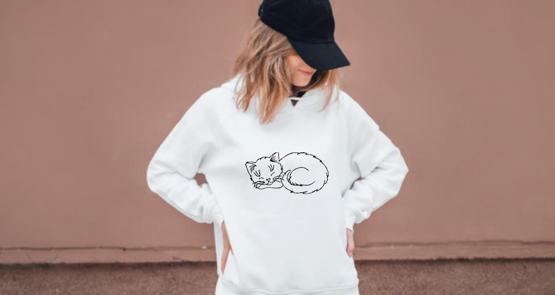 Puede incluir: Una sudadera blanca con un contorno negro de un gato durmiendo en la parte delantera.