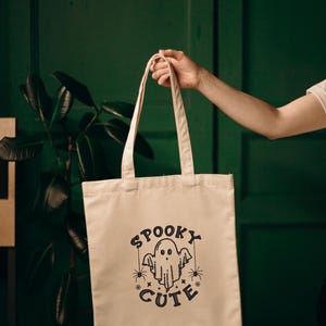 May include: A white tote bag with a black design of a ghost with the text "Spooky Cute" and spiders.