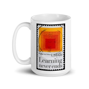 May include: White ceramic mug featuring a postage stamp design with a series of orange and red squares. The stamp reads "Learning never ends" in black text. The mug has a white handle and a glossy finish.