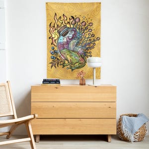 May include: A yellow tapestry with a colorful illustration of a frog, mushrooms, and a potion bottle. The artwork features a detailed design with vibrant colors and a whimsical theme. The tapestry is displayed above a wooden dresser.