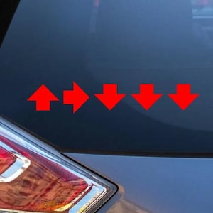 May include: A set of five red arrow decals applied to a dark vehicle window. The first arrow points upward, the second points to the right, and the remaining three arrows point downward, arranged in a horizontal line across the glass surface.