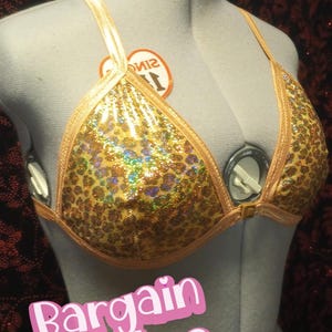 May include: A gold sequined bikini top with a leopard print design. The top has thin straps and a clasp closure. The text "Bargain Babes" is displayed in a pink font.