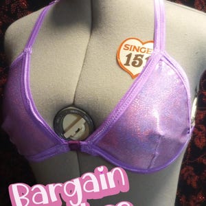 May include: A lavender bikini top with a shimmering, glittery finish. The top is displayed on a mannequin and features a halter neck design. The words "Bargain Babes" are in a pink font across the bottom of the image.