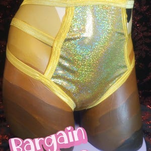 May include: A pair of high-waisted bottoms with a shimmering gold front panel and yellow trim. The bottoms are displayed on a mannequin with a gradient of brown tones. The text "Bargain Babes" is visible at the bottom.