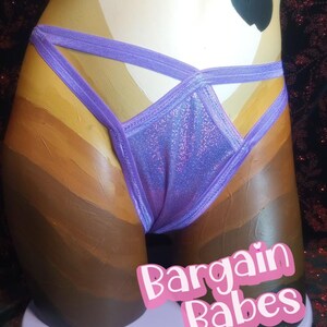 May include: A purple, glittery lingerie bottom with crisscross straps is displayed on a mannequin. The mannequin is painted with a gradient of skin tones. The text "Bargain Babes" is in pink on a white background.