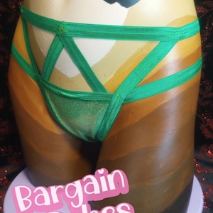 Puede incluir: Conjunto de lencería verde con diseño de tiras. Se muestra en un maniquí con un degradado de tonos de piel. El texto "Bargain Babes" es visible en la parte inferior. Un gráfico de corazón negro en la parte superior.