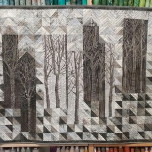 Könnte beinhalten: Eine Steppdecke mit einem geometrischen Muster aus Dreiecken in Grautönen, Weiß und Schwarz. Die Steppdecke zeigt im Zentrum ein Baummotiv, das eine Waldszene erzeugt.