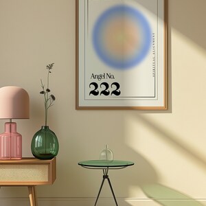 May include: A framed poster with a blurred blue, yellow, and orange circle in the center. The poster has the text "Angel No. 222" and "Spiritual Alignment" on it. The poster is hanging on a light beige wall with a wooden floor and a black and white checkered rug.