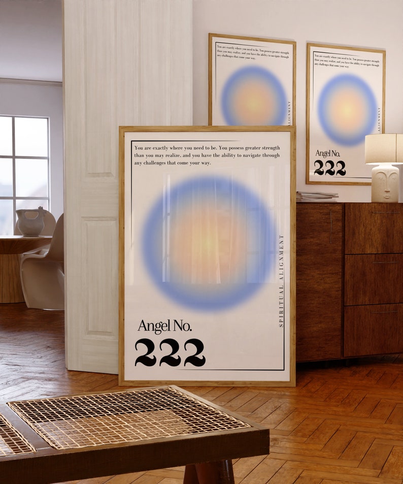 May include: A white poster with a blue and orange gradient circle in the center. The poster has the text "Angel No. 222" and the text "Spiritual Alignment" on the right side. The poster is framed in wood and hanging on a wall.