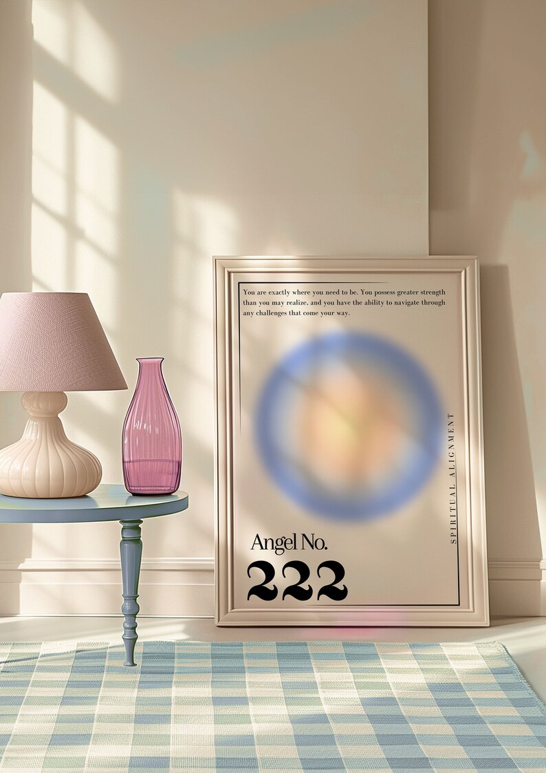 May include: A framed poster with a blurred image of a circle in the center. The poster has the text "Angel No. 222" and "Spiritual Alignment" on it. The poster is sitting on a table with a pink lamp and a pink glass vase.