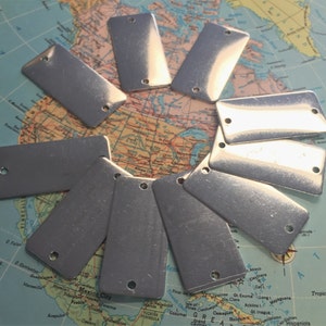 May include: Ten silver rectangular metal tags with rounded corners and two holes in each tag. The tags are arranged in a circle on a map.