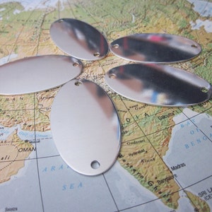May include: Five silver-colored, oval-shaped metal tags with a hole at each end. The tags are reflective and lie on a map of the world, with the Middle East and India visible.