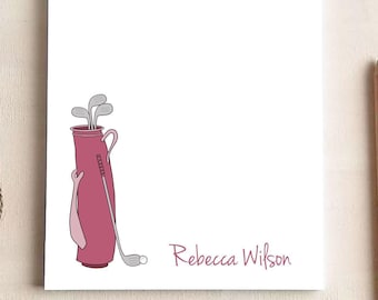 May include: A white rectangular notepad featuring a pink golf bag illustration with grey golf clubs and a golf ball. The name Rebecca Wilson is printed in pink text in the bottom right corner of the paper sheet.