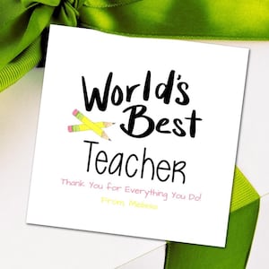 Puede incluir: Una tarjeta blanca con texto negro que dice "World's Best Teacher" con dos l&aacute;pices amarillos cruzados. El texto "Thank You for Everything You Do!" est&aacute; escrito en rosa debajo del texto principal. El texto "From Melissa" est&aacute; escrito en amarillo debajo del texto rosa.