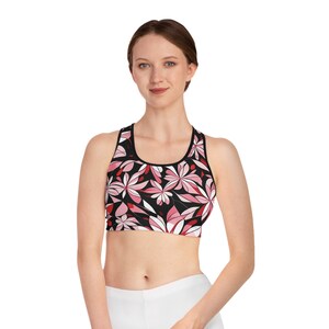 Könnte beinhalten: Schwarzer Sport-BH mit einem Blumenmuster in Rosa- und Rottönen. Der BH hat einen Rundhalsausschnitt und ein Racerback-Design. Das Blumenmuster ist vor einem schwarzen Hintergrund platziert. Der BH besteht aus einem weichen, dehnbaren Material.