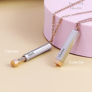 Op de afbeelding: Twee zilveren kettingen met gepersonaliseerde naamplaatjes. De ene ketting heeft een cilinderbedel met de naam "Mark" erop gegraveerd. De andere ketting heeft een kubusvormige bedel met de naam "Charles" erop gegraveerd.