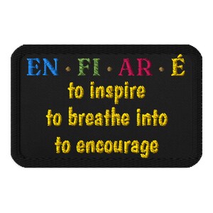 Könnte beinhalten: Ein rechteckiger, schwarz bestickter Aufnäher mit genähtem Rand. Die oberste Zeile zeigt den mehrfarbigen Text EN • FI • AR • É. Darunter befindet sich der gelb gestickte Text to inspire, to breathe into und to encourage.