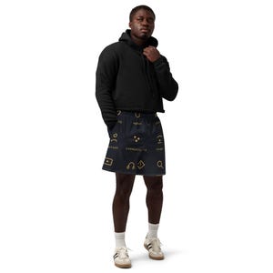 May include: A black cropped hoodie with long sleeves and a drawstring hood, paired with dark navy blue shorts featuring a repeating pattern of gold-colored icons and text including the words water, person, community, and stage.