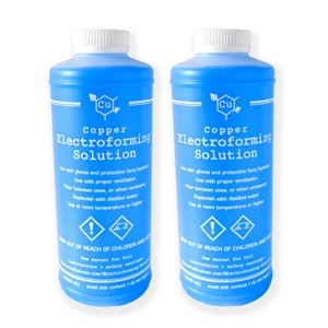 May include: Two blue plastic bottles of Copper Electroforming Solution with white caps. The bottles have white text with instructions and warnings. The bottles are for electroforming projects.