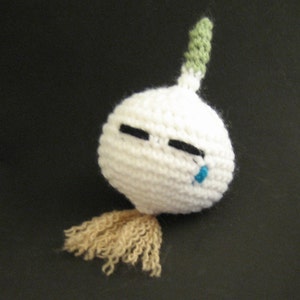 Peut inclure: Une gousse d'ail en crochet blanc avec une tige verte et une larme bleue. L'ail a une barbe en laine brune.
