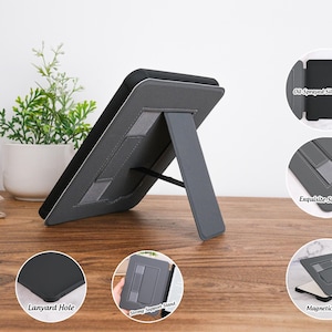 May include: A gray tablet case with a built-in stand. The case features a lanyard hole, oil-sprayed silicone, exquisite stitching, a strong support stand, and a magnetic back. The tablet is propped up on a wooden surface.