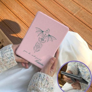 Puede incluir: Una funda rosa para tableta con un diseño de espada, alas y luna y el texto "you do not yield, Francisco". La funda está en las manos de una persona. La funda tiene un soporte.