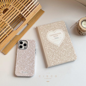 May include: A white phone case with a speckled pattern and the word "Cisco" printed on it. The case is next to a composition book with a heart-shaped design and the words "Composition Book Cisco" printed on it.