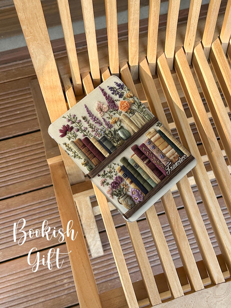 May include: A decorative book-themed item featuring embroidered flowers and books. The item is rectangular with a light-colored background and a brown border. The text "Bookish Gift" is visible in the image.