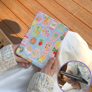 Può includere: Una custodia per tablet azzurra con illustrazioni colorate di frutta e verdura in scatola. La custodia presenta disegni di carote, fragole e arance. Il testo "Francesco's Kindle" è stampato sulla custodia.