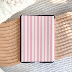 Puede incluir: Un dispositivo lector electr&oacute;nico rectangular con una funda protectora que presenta un patr&oacute;n de rayas verticales en tonos alternos de rosa claro y blanco. El dispositivo tiene un marco negro delgado que rodea el &aacute;rea de la pantalla.