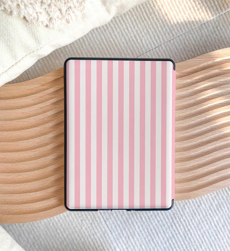 Puede incluir: Un dispositivo lector electr&oacute;nico rectangular con una funda protectora que presenta un patr&oacute;n de rayas verticales en tonos alternos de rosa claro y blanco. El dispositivo tiene un marco negro delgado que rodea el &aacute;rea de la pantalla.
