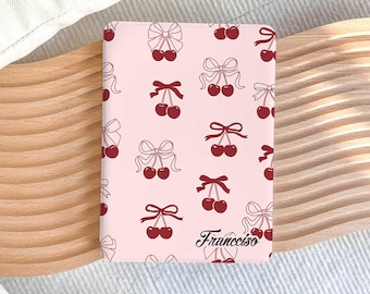 Puede incluir: Una cubierta de cuaderno rosa con un patrón repetido de cerezas rojas y lazos blancos. El texto "Francesco" está impreso en negro en la parte inferior de la cubierta.