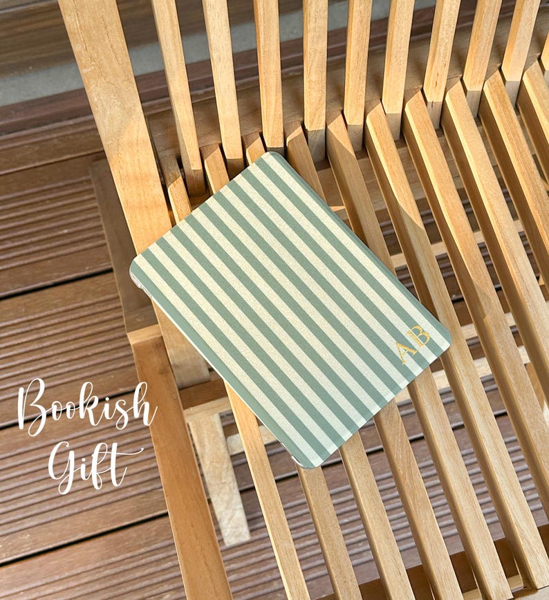 Puede incluir: Un cuaderno rectangular con un patr&oacute;n de rayas verticales en verde salvia y blanco. La cubierta muestra las iniciales AB en color dorado en la esquina inferior derecha. El texto Bookish Gift est&aacute; impreso en blanco a la izquierda.