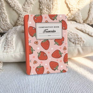 Könnte beinhalten: Ein rosa Hefter mit einem Erdbeer- und Sternenmuster. Der Hefter hat einen roten Rücken und den Text "COMPOSITION BOOK" und "Francesco" auf dem Einband.