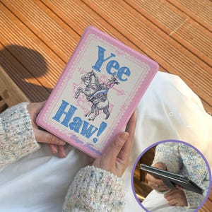 May include: Pink rectangular case with the words "Yee Haw!" and a graphic of a horse and rider. The case has a decorative border and the text "Slayer Francisco".