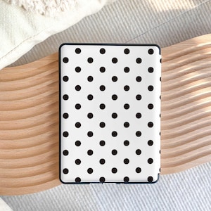 Puede incluir: Un dispositivo lector electr&oacute;nico rectangular con una cubierta trasera blanca adornada con un patr&oacute;n repetitivo de peque&ntilde;os puntos negros s&oacute;lidos. El dispositivo tiene un marco fino de color oscuro que rodea la superficie blanca.