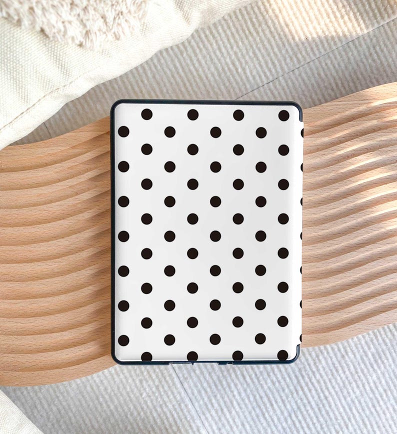 Puede incluir: Un dispositivo lector electr&oacute;nico rectangular con una cubierta trasera blanca adornada con un patr&oacute;n repetitivo de peque&ntilde;os puntos negros s&oacute;lidos. El dispositivo tiene un marco fino de color oscuro que rodea la superficie blanca.