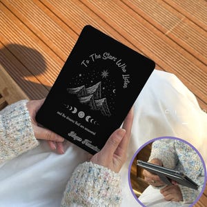 Könnte beinhalten: Schwarze Tablet-Hülle mit Berg- und Mondphasen-Design. Die Hülle trägt den Text "To The Stars Who Listen" und "and the dreams that are answered". Die Hülle wird von einer Person in den Händen gehalten.