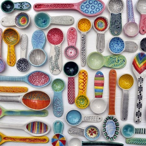 May include: A collection of colorful hand-painted ceramic spoons with various patterns and designs. The spoons are all different shapes and sizes, and some have words written on them, such as "Coffee".