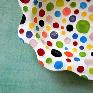 May include: A white ceramic bowl with a scalloped edge and a polka dot pattern in various colors, including red, green, blue, yellow, and pink.