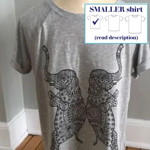 May include: Gray t-shirt featuring a black and white design of two elephants facing each other. The elephants are intricately patterned. The shirt has rolled-up sleeves and the text "SMALLER shirt" in a box.