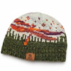 May include: A knit beanie featuring a forest green ribbed brim and a landscape pattern. The design displays a dark green tree line, a vibrant orange and purple sunset, and a light blue sky with small star-like motifs. A brown leather tag reads hand made.