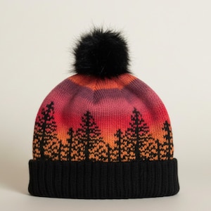 May include: A knitted beanie with a black pom-pom. The hat features a black ribbed brim and a colorful design of a sunset with trees in shades of red, orange, and purple.