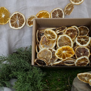 May include: A cardboard box filled with dried orange slices. The box is sitting on a white fabric surface with a garland of dried orange slices.