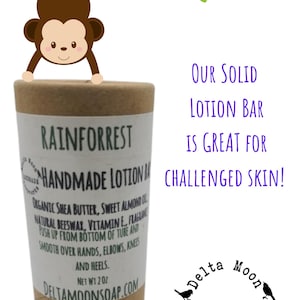 May include: A brown cardboard tube with a white label that reads "Rainforest Handmade Lotion Bar". The label lists ingredients including shea butter, sweet almond oil, beeswax, vitamin E, and fragrance. The label also says "Push up from bottom of tube and smooth over hands, elbows, knees and heels. Net Wt 2 oz. DeltaMoonSoap.com". The tube is sitting on a white background with a cartoon monkey hanging from a branch.